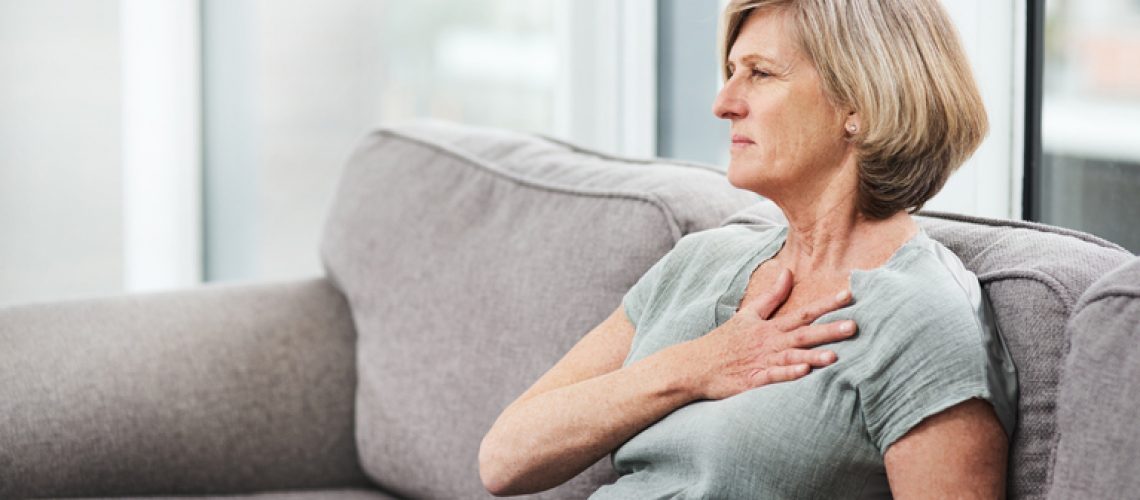 Shot of a senior woman suffering from chest pain while sitting on the sofa at home